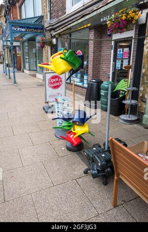 Bunte Gießkannen aus Kunststoff vor einem Eisenwarenladen. Stockfoto