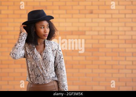 Porträt einer stilvollen Frau mit einem schwarzen Hut auf einem Backsteinwand Hintergrund Stockfoto