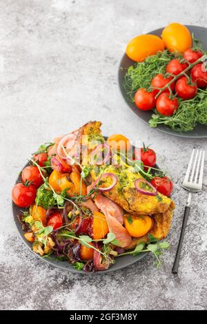 Omelette mit geschmortem Gemüse und Lachs, Tomaten mit Zwiebeln, Brokkoli und rotem Fisch mit Erbsen-Microgreens, leckeres herzhaftes Frühstück Stockfoto