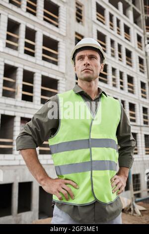 Vertikales Porträt eines jungen männlichen Ingenieurs, der auf der Baustelle posiert Stockfoto