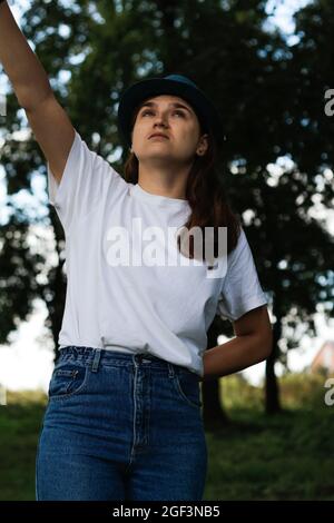 Unschärfe-Nahaufnahme Porträt einer traurigen jungen Frau mit braunen Haaren trägt einen Hut im Freien. Grüne Natur Hintergrund. Suchen nach oben. Frauen stehen im Dunkeln Stockfoto