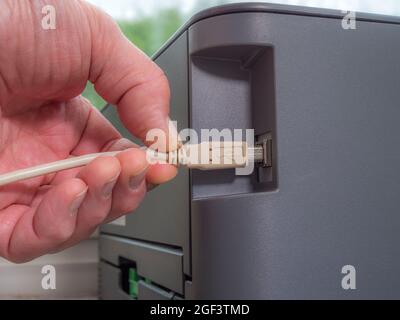 Nahaufnahme eines Mannes, der ein Kabel/Kabel in die USB-Buchse eines Computerdruckers gesteckt hat. Stockfoto