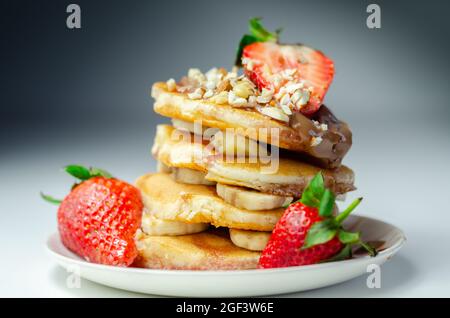 Pfannkuchen mit Bananen, Erdbeeren und Nüssen, gekrönt mit Schokolade und Erdbeersoße, süßes Frühstück Stockfoto