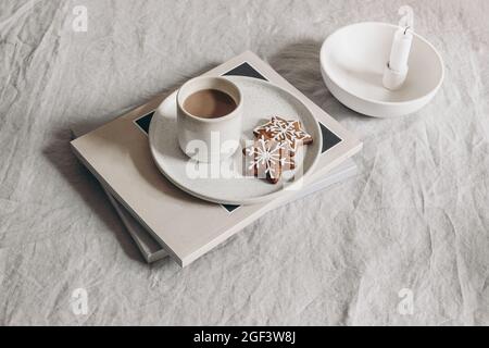 Winter festliche Stillleben Szene. Tasse Kaffee auf Zeitschriften. Stern-Lebkuchen auf beigefarbenem Keramikteller. Frühstückstisch mit beigefarbenen Leinentücher Stockfoto