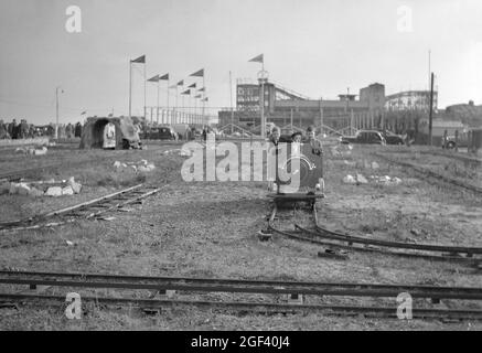 Die Miniatureisenbahn an der Strandpromenade von Felixstowe, Suffolk, England in den 1950er Jahren. Die Kinder befinden sich in ihrem eigenen Eisenbahnmotor, der von einem Elektromotor angetrieben wird, der seine Ladung von der 3-Schienen-Strecke übernimmt. Der ‘Landschaft’ steht auf der Vergnügungsfahrt nur sehr wenig im Weg, außer einem ‘Tunnel’ (links im Hintergrund). Der Veranstaltungsort Mannings mit seiner großen Dipper-Fahrt liegt in der Ferne. Dies stammt aus einem Schwarz-Weiß-Negativ, das von einem Amateurfotografen aufgenommen wurde – einem Vintage-Foto aus den 1950er Jahren. Stockfoto