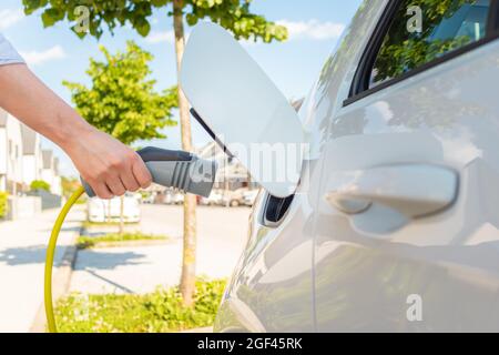 Weibliche Hände, die die Kappe der Ladestation für Elektroautos öffnen und ein Ladegerät anschließen Stockfoto