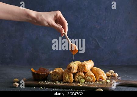 Frau gießt Honig auf köstlichen Baklava auf dunklem Hintergrund Stockfoto