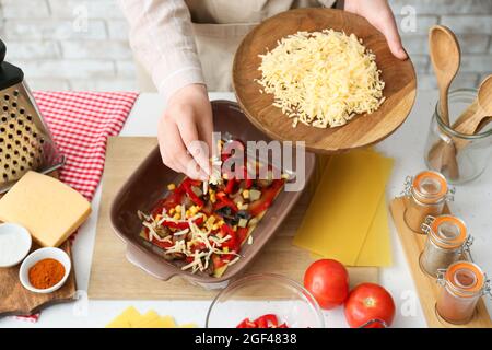 Frau bereitet leckere Tomatenlasagne mit Gemüse und Käse am Tisch in der Küche, Nahaufnahme Stockfoto
