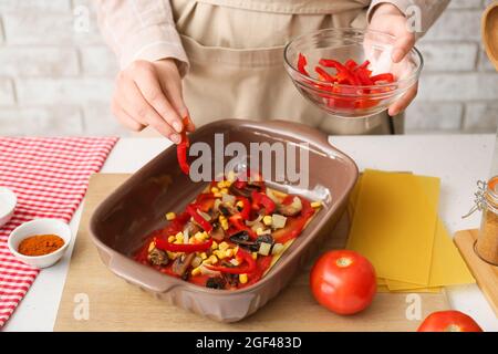 Frau bereitet leckere Tomatenlasagne mit Gemüse am Tisch in der Küche, Nahaufnahme Stockfoto