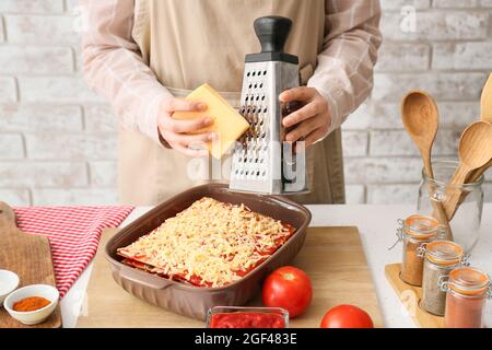 Frau, die Käse in die Backform mit leckeren Tomatenlasagne am Küchentisch gab, Nahaufnahme Stockfoto