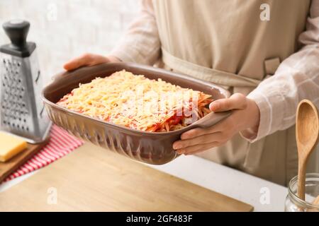 Frau hält eine Auflaufform mit leckeren Tomatenlasagne am Tisch in der Küche, Nahaufnahme Stockfoto