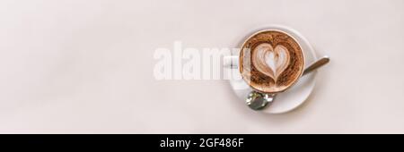 Latte Art Kaffeebecher von oben am Kaffeetisch mit weißem Hintergrund und Panoramafanner mit herzförmigem Schaumstoff von Barista Stockfoto