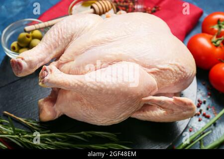 Brett mit ganz rohem Huhn und Gewürzen auf farbigem Hintergrund, Nahaufnahme Stockfoto