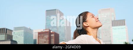 Happy healthy woman taking deep breath in city clean air for pollution concept panoramic lansdcape header banner. Asian lady in Asia face portrait Stockfoto