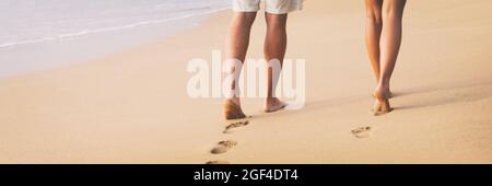 Strandpaar, das barfuß auf Sand beim Sonnenuntergang spazieren geht, wandern auf dem Hochzeitsreise-Banner - Frau und Mann entspannen sich zusammen und hinterlassen Fußabdrücke im Sand. Stockfoto