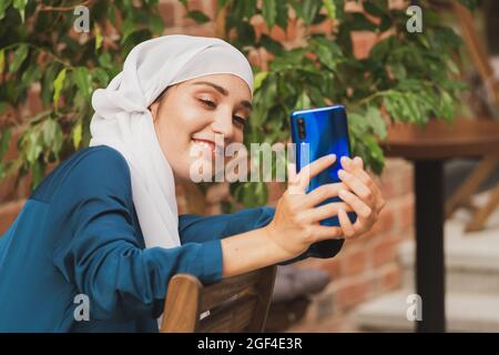 Muslimische Frau nimmt Selfie. Glücklich schönes Mädchen mit Schal nehmen Sie ein Bild von sich selbst mit dem Smartphone. Stockfoto
