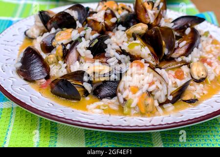 Gekochter Reis, Risotto mit Muscheln und Garnelen auf einem Teller auf einem bunten Handtuch Stockfoto