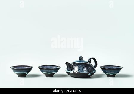 Grüner Tee in einer dunkeltürkisfarbenen Teekannen aus Ton und kleine Tassen auf pastellfarbenem Hintergrund. Kreatives minimalistisches Konzept für Teezeremonien. Speicherplatz kopieren. Stockfoto
