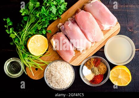 Eine Pfanne Spanisches Huhn und Reis Zutaten: Rohe Hühnerschenkel, Reis, Gewürze und andere Zutaten auf einem Holztisch Stockfoto