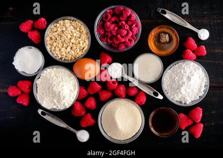 Zutaten für Himbeer-gebackene Donuts mit Himbeer-Glasur: Himbeeren, Mehl, Zucker und andere ungekochte Zutaten auf dunklem Holzgrund Stockfoto