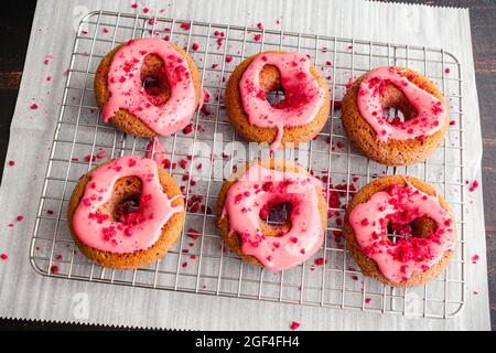 Himbeer-gebackene Donuts mit Himbeer-Glasur auf einem Wire Cooling Rack: Gebackene Donuts mit rosa Himbeer-Glasur und roten Streuseln Stockfoto