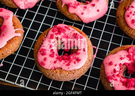 Himbeer-gebackene Donuts mit Himbeer-Glasur auf einem Wire Cooling Rack: Gebackene Donuts mit rosa Himbeer-Glasur und roten Streuseln Stockfoto