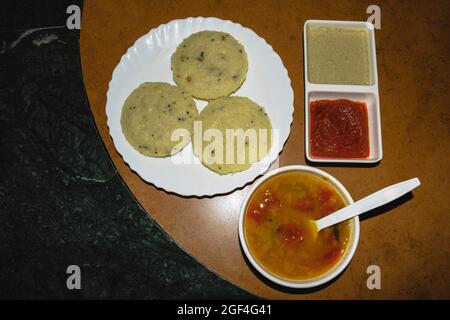 Beliebtes südindisches Frühstück Rava idli mit hausgemachtem Sambar und zwei Arten von Chutney, weißem Chutney und Rot auf dem Tisch serviert Stockfoto