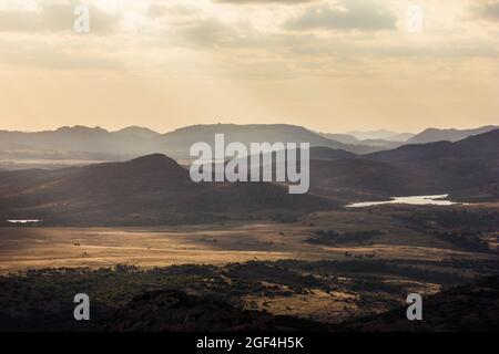 Weitwinkelaufnahme von Bergen bei Sonnenuntergang, eine grüne Berglandschaft im Hintergrund mit orangefarbenem Sonnenaufgangshimmel Stockfoto