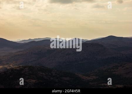 Weitwinkelaufnahme von Bergen bei Sonnenuntergang, eine grüne Berglandschaft im Hintergrund mit orangefarbenem Sonnenaufgangshimmel Stockfoto