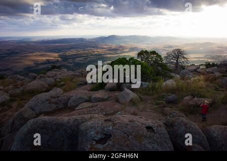 Weitwinkelaufnahme oder Hintergrund einer dramatischen geschichteten Landschaft aus felsigen Bergen mit Bäumen bei Sonnenuntergang Stockfoto