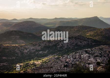 Weitwinkelaufnahme oder Hintergrund einer dramatischen geschichteten Landschaft aus felsigen Bergen mit Bäumen bei Sonnenuntergang Stockfoto