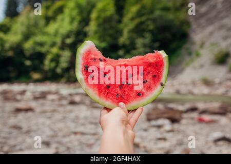 Frau hält ein Stück Wassermelone in der Hand auf dem Berg im Freien. Snacks, die im Sommer auf Reisen gegessen werden. Stockfoto