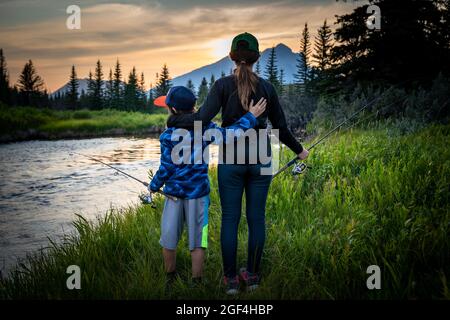 Bruder und Schwester stehen neben einem Bach, während sie in Alberta, Kanada, bei Sonnenuntergang angeln. Stockfoto