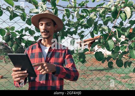 Schwarzer Mann Bauer hält eine Tablette mit Hut auf dem Bauernhof, Passionsfrucht Pflanze im Hintergrund. Stockfoto