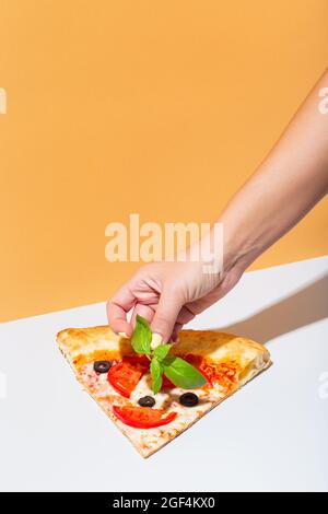 Frau legt Basilikum auf eine Scheibe Pizza. Hausgemachte italienische Pizza mit Oliven, Tomaten und Basilikum Stockfoto