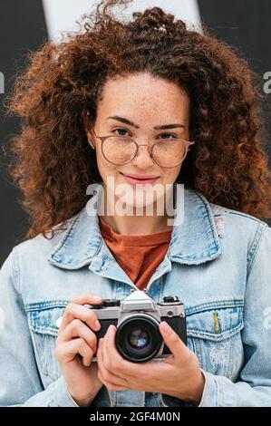 Selbstbewusste junge lockige Frau mit Kamera Stockfoto