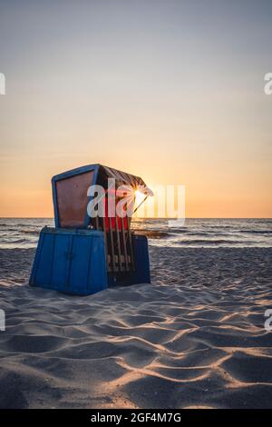 Strandstuhl mit Kapuze, der bei Sonnenuntergang am sandigen Küstenstrand steht Stockfoto