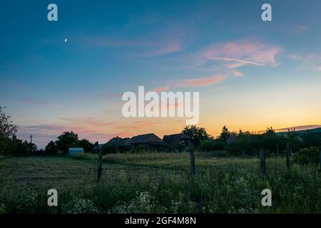 Lila Wolken mit Mond über der rumänischen Landschaft in der Dämmerung Stockfoto