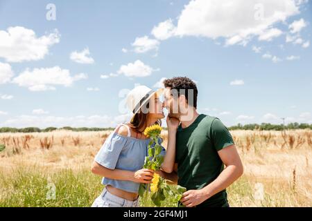 Lächelndes Paar mit Sonnenblumen, die an sonnigen Tagen die Nase reiben Stockfoto