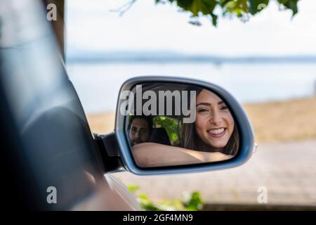 Spiegelung eines lächelnden Paares auf dem Seitenspiegel Stockfoto