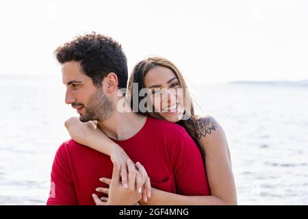 Lächelnde Frau umarmt den Mann von hinten Stockfoto