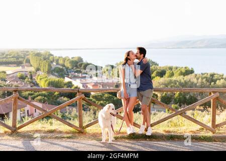 Freund küsst Freundin, während lehnte sich auf Geländer von Hund Stockfoto