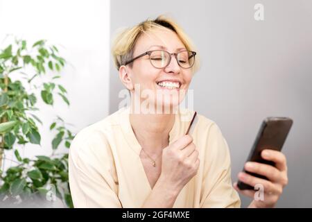 Lächelnde Frau, die zu Hause über das Mobiltelefon online mit der Kreditkarte einkaufen kann Stockfoto