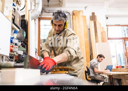 Handwerker, die Ohrschützer tragen und während der Arbeit von Kollegen in der Werkstatt schreiben Stockfoto