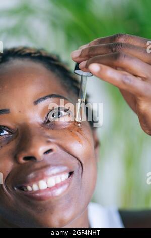 Afro-Frau lächelt, während sie das Gesichtsserum durch die Pipette auftragen Stockfoto