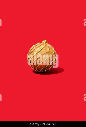 Studioaufnahme eines einzigen goldfarbenen Weihnachtsornaments, das auf einem leuchtend roten Hintergrund liegt Stockfoto