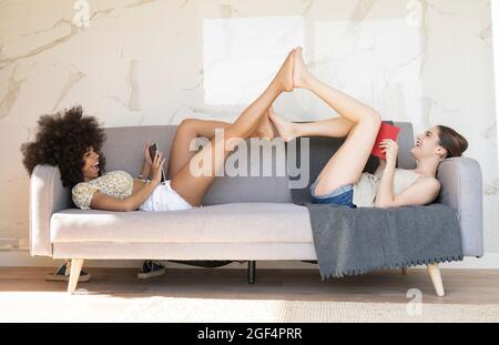 Lächelnde Freundinnen liegen zu Hause auf dem Sofa zusammen Stockfoto