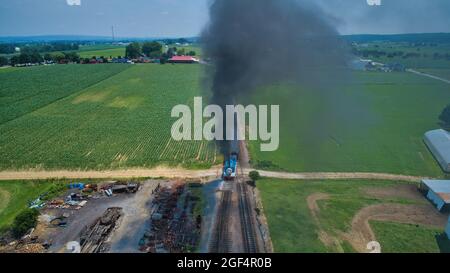Ronks, Pennsylvania, Juni 2019 - Luftkopf mit Blick auf Thomas, den Panzermotor, der sich an einem schönen Sommertag durch Bäume und Ackerland nähert und Pkw zieht, die Rauch aufblasen Stockfoto