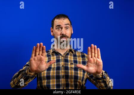 Fröhlich öffnete ein fröhlicher Mann mit einem karierten Hemd seinen Mund weit und zeigt Palmen auf blauem Hintergrund Stockfoto