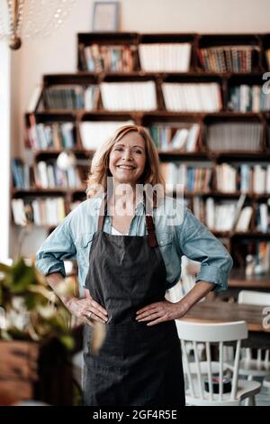 Glückliche weibliche Cafe-Besitzerin, die mit der Hand auf der Hüfte steht Stockfoto
